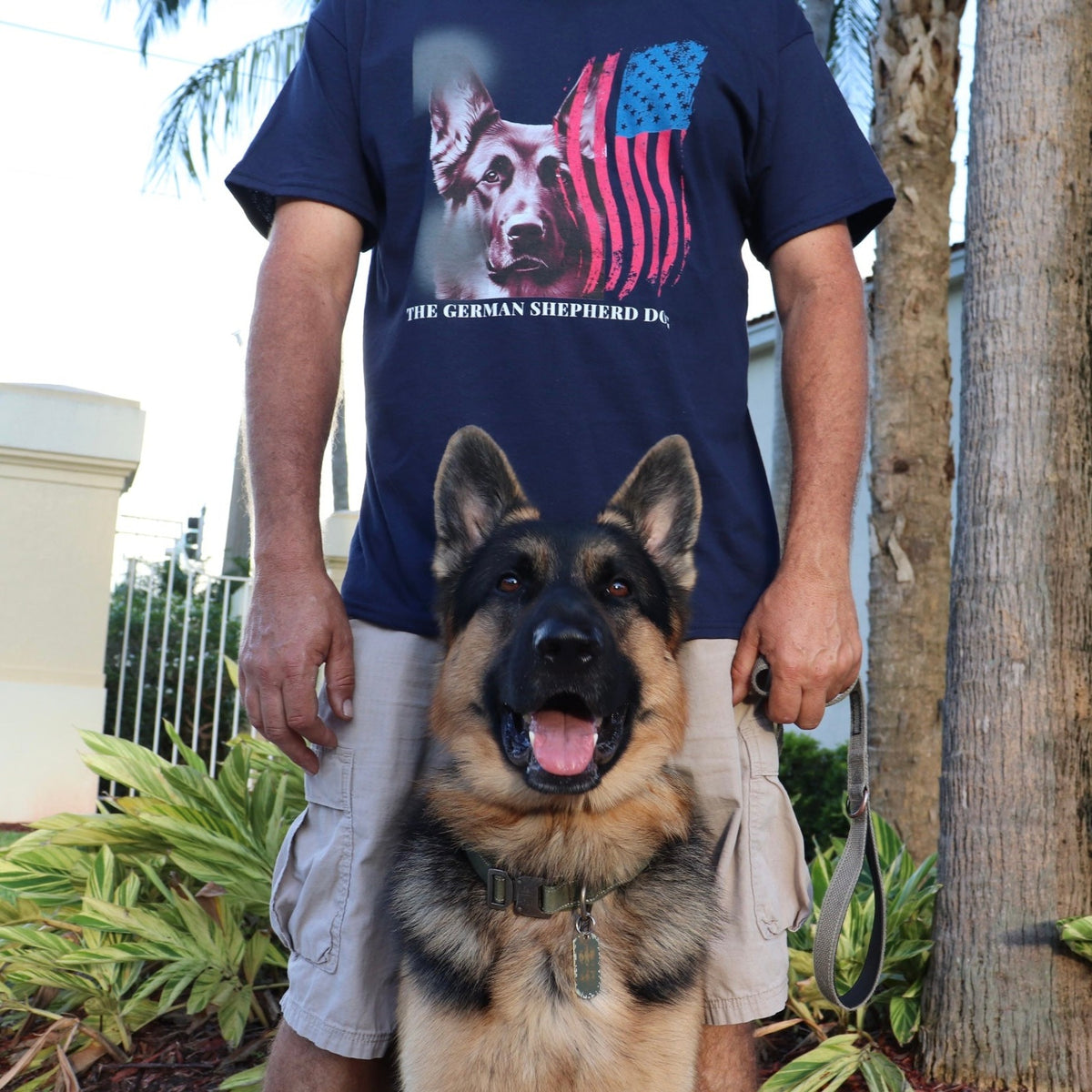 Man wearing navy patriotic German Shepherd t-shirt outdoors with his German Shepherd dog